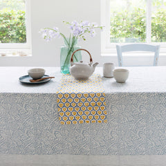 Kitchen table covered with a table cloth and laid with tea cups, a tea pot and a vase of flowers 